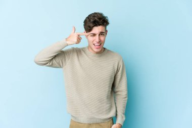 Mavi arka planda izole edilmiş genç beyaz adam işaret parmağıyla bir hayal kırıklığı jesti gösteriyor..