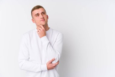 Beyaz arka planda genç beyaz bir adam şüpheli ve şüpheci bir ifadeyle yana bakıyor..