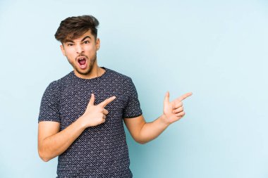 Mavi arka planda izole edilmiş genç bir Arap adam işaret parmağıyla fotokopi alanını işaret ederek heyecan ve arzuyu ifade ediyor..