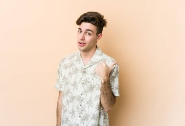 Beyaz tenli genç adam bej arka planda izole edilmiş, başparmak uzakta, gülüyor ve kaygısız..