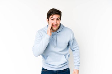 Beyaz arka planda izole genç adam yüksek sesle bağırıyor, gözleri açık ve elleri gergin tutuyor..