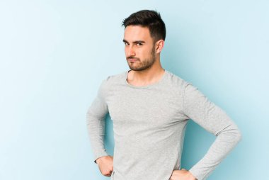 Kafkasyalı genç adam mavi arka planda izole edilmiş hoşnutsuzca kaşlarını çatmış, kollarını kavuşturmuş..
