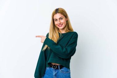 Beyaz arka planda izole edilmiş genç sarışın kadın gülümsüyor ve boş alanda bir şeyler gösteriyor..