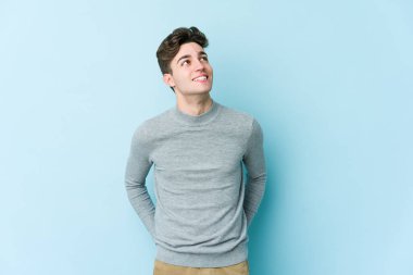 Kafkasyalı genç adam mavi arka planda izole edilmiş rahat ve mutlu bir şekilde gülüyor, boynunda dişlerini gösteriyor..