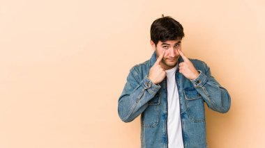 Bej arka planda izole edilmiş genç adam ağlıyor, bir şeyden memnun değil, acı ve kafa karışıklığı konsepti..