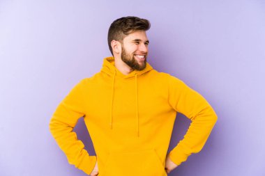 Mor arka planda izole edilmiş genç adam mutlu bir şekilde gülüyor ve ellerini karnının üstünde tutarak eğleniyor..