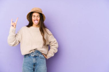 Mor arka planda izole edilmiş genç beyaz kadın parmaklarıyla taş hareketi gösteriyor.