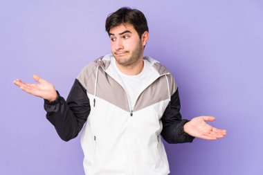 Mor arka planda izole edilmiş genç bir adam. Kafası karışmış ve omuz silkiyor. Kopya alanını tutmak için..