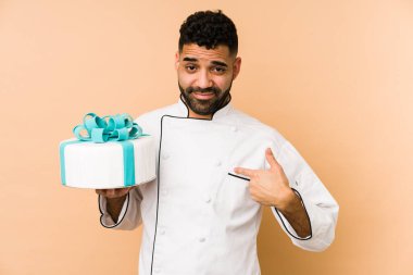 Genç, latin fırıncı, izole edilmiş bir pasta tutuyor. Seni işaret ediyor. Sanki seni davet ediyormuş gibi..