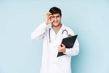 Genç doktor, mavi arka planda izole edildi. Heyecanlı görünüyor..