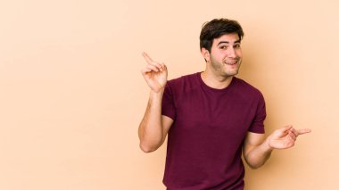 Bej arka planda izole edilmiş genç adam farklı kopya alanlarını gösteriyor, birini seçiyor, parmaklarıyla gösteriyor.