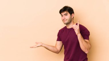 Bej arka planda izole edilmiş genç bir adam elinde bir ürün tutuyor..