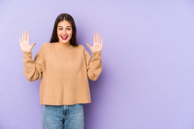 Mor arka planda izole genç beyaz kadın hoş bir sürpriz alıyor, heyecanlı ve el kaldırıyor..