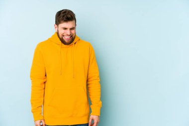 Mavi arka planda izole edilmiş genç beyaz adam gülüyor ve gözlerini kapıyor, rahatlamış ve mutlu hissediyor..