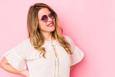 Pembe arka planda gözlüklü genç beyaz kadın sırt ağrısı çekiyor..