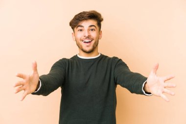 Bej bir arka planda izole edilmiş genç bir Arap adam kameraya sarıldığı için kendinden emin hissediyor..