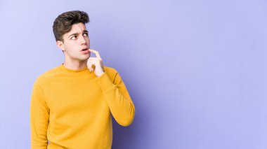 Mor arka planda izole edilmiş genç beyaz adam şüpheli ve şüpheci bir ifadeyle yana bakıyor..