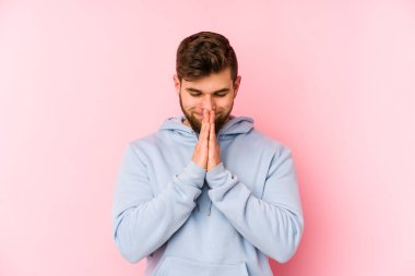 Pembe arka planda izole edilmiş genç beyaz bir adam. El ele tutuşup, ağız kenarında dua ediyor. Kendine güveniyor..
