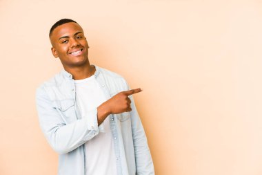Genç Latin adam bej arka planda izole edilmiş gülümseyen ve işaret eden boş alanda bir şey gösteriyor..