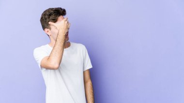 Mor arka planda izole edilmiş genç beyaz adam elleriyle gözlerini kapatıyor, geniş bir gülümsemeyle bir sürpriz bekliyor..