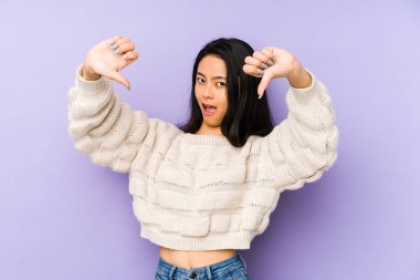 Mor bir arka planda izole edilmiş genç Çinli kadın baş parmağını aşağı gösteriyor ve hoşlanmadığını ifade ediyor..