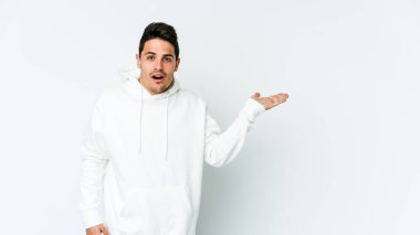 Beyaz arka planda izole edilmiş genç beyaz adam, avuç içi fotokopi alanını elinde tutmaktan etkilenmiş..