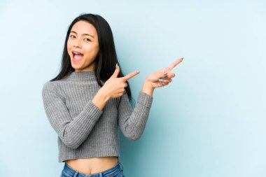 Mavi bir arka planda izole edilmiş genç Çinli kadın işaret parmaklarıyla fotokopi alanını işaret ederek heyecan ve arzusunu ifade ediyor..