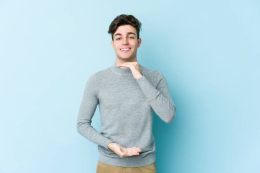 Mavi arka planda izole genç beyaz adam iki eliyle bir şey tutuyor, ürün sunumu..