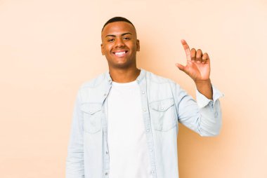 Genç Latin bir adam bej arka planda izole edilmiş. Elinde küçük bir işaret parmağı olan, gülümseyen ve kendinden emin bir şey tutuyor..