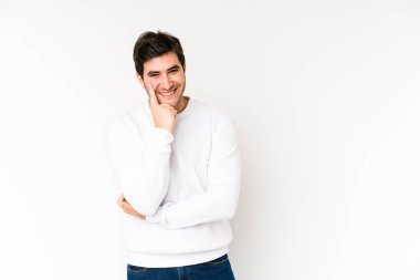 Beyaz arka planda izole edilmiş genç adam gülümsüyor mutlu ve kendinden emin, elleriyle çeneye dokunuyor..