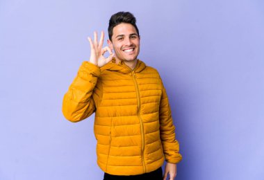 Genç beyaz adam mor arka planda izole edilmiş neşeli ve kendinden emin, iyi bir jest yapıyor..