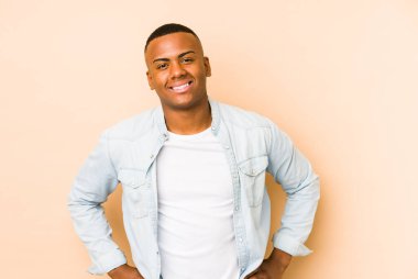 Genç Latin adam bej arka planda izole edilmiş. Kendine güveniyor. Kalçaları tutuyor..