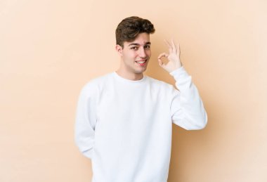 Beyazlı genç bir adam bej arka planda izole edilmiş bir şekilde göz açıp kapayıncaya kadar elinde iyi bir el hareketi tutuyor..