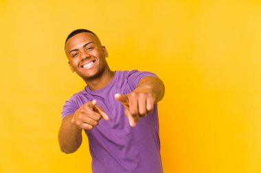 Sarı arka planda izole edilmiş genç latin adam öne bakan neşeli gülümsemeler.