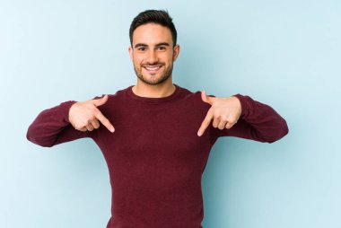 Kafkasyalı genç adam mavi arka planda izole edildi. Parmakları aşağıda, olumlu bir his var..