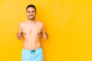 Sarı arka planda mayosu olan genç beyaz bir adam. İki eliyle bir şey tutan beyaz bir adam. Ürün sunumu..