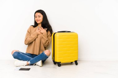 Yerde, izole edilmiş bir bavulla oturan Çinli genç bir yolcunun, avuçlarını göğsüne bastıran dostane bir ifadesi vardır. Aşk konsepti.
