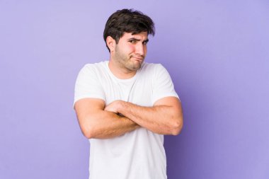Mor arka planda izole edilmiş, hoşnutsuzca kaşlarını çatmış, kollarını kavuşturmuş genç bir adam..