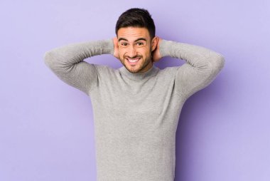 Kafkasyalı genç bir adam mor arka planda izole edilmiş kafasının arkasına dokunuyor, düşünüyor ve bir seçim yapıyor..