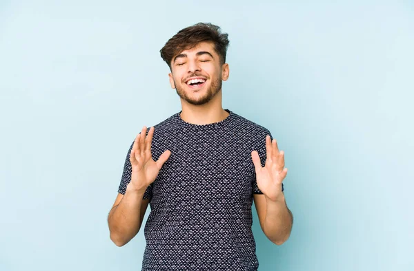 Genç Arap bir adam mavi bir arka planda izole edilmiş neşeli bir şekilde gülüyor. Mutluluk kavramı.