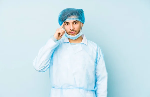 年轻的阿拉伯外科医生 被隔离在蓝色的背景下 用手指 专注于一项任务 指向圣殿 — 图库照片