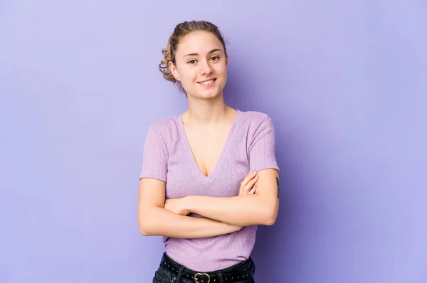 Young caucasian woman on purple background who feels confident, crossing arms with determination.