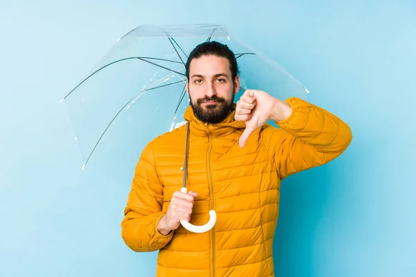 若い男は長い髪を見て傘を持って隔離された嫌いなジェスチャーを示すを着て 親指を下に 意見の相違 — ストック写真