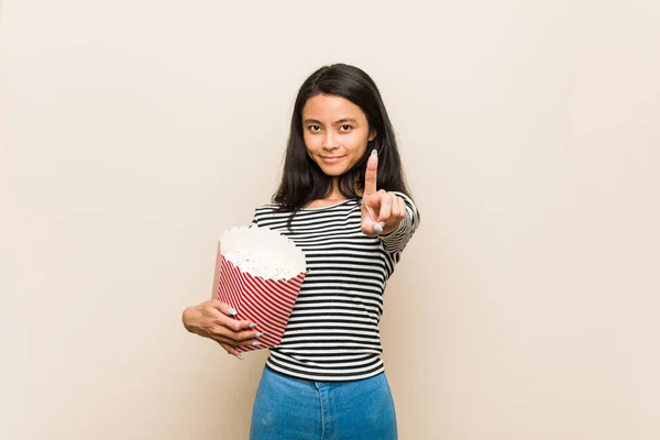 年轻的亚洲女孩拿着一个爆米花桶 用手指显示头号爆米花 — 图库照片