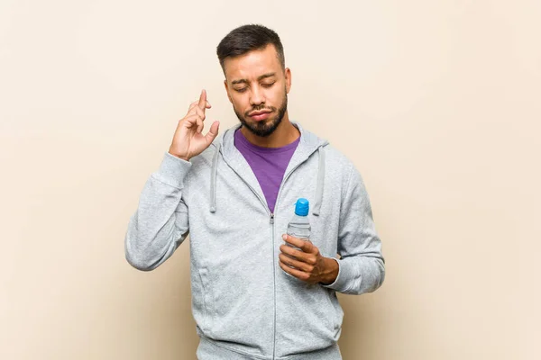 Jovem Mestiço Asiático Homem Segurando Uma Garrafa Água Cruzando Dedos — Fotografia de Stock