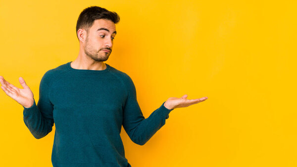 Молодой кавказский человек, изолированный на желтой пекарне, смущен и сомнительно пожимает плечами, чтобы держать пространство для копирования..