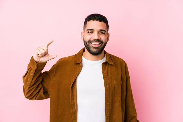 Jovem Latino Contra Fundo Rosa Isolado Segurando Algo Pouco Com — Fotografia de Stock