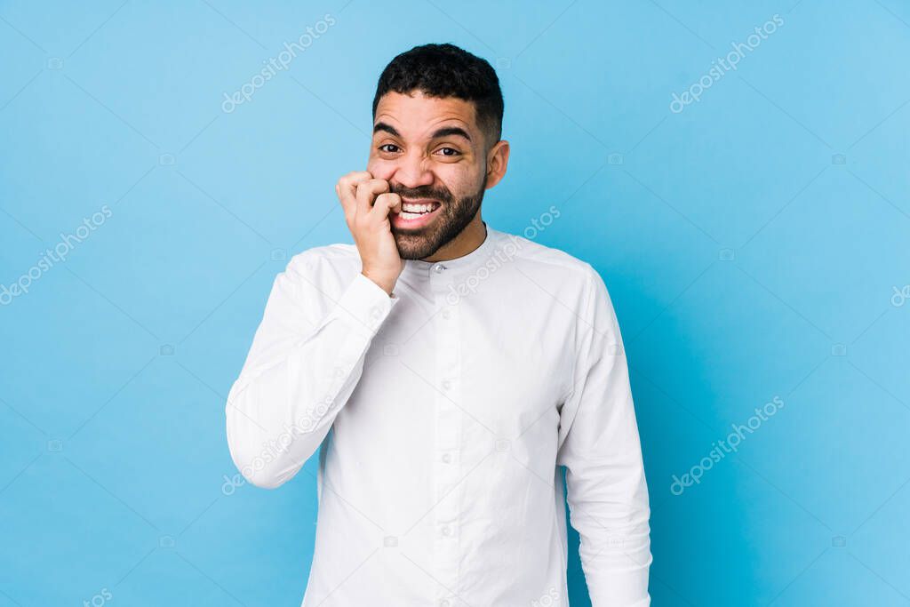 Young latin man against a blue  background isolated biting fingernails, nervous and very anxious.
