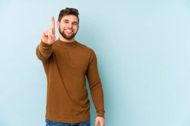 Mavi arka planda izole edilmiş genç beyaz adam bir numarayı parmağıyla gösteriyor..