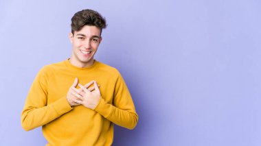 Mor arka planda izole edilmiş beyaz bir genç, dost bir ifadeye sahip, avuçlarını göğsüne bastırıyor. Aşk konsepti.